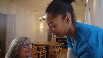 Caring female nurse assists senior woman in wheelchair with getting dressed in a cozy home living room, offering compassionate support, companionship and gentle elderly care