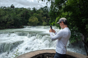 A male tourist admires and photographs the El Meco waterfall surrounded by lush green forest in Mexico&rsquo;s Huasteca region, San Luis Potosi, Mexico.