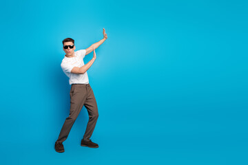 Stylish young man in casual wear posing confidently against bright blue background, wearing sunglass and gesturing with hands