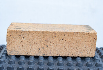 Firebrick on dark dimpled drainage membrane, close up of heat resistant ceramic used for thermal insulation, foundation damp proofing, and high temperature construction applications
