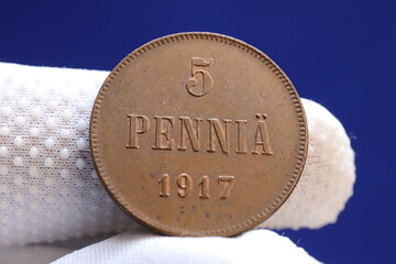 A close-up of a vintage coin displaying the denomination '5 PENNIÄ' and the year '1917', held by a...