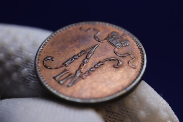 A close-up of an antique coin held by a gloved hand, featuring intricate engravings and a crown design
