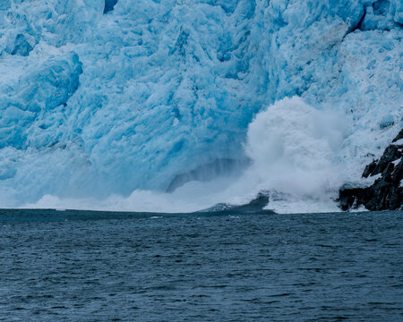 Calving action at Aialak Glacier causes a massive sea swell crashing into rocks