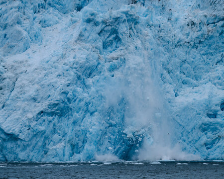 Aialik Glacier face calving ice bergs into the bay with seabirds flying in front of the mountainous spray of the splash provides perspective on its size