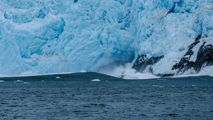 Calving action at Aialak Glacier causes a massive sea swell crashing into rocks