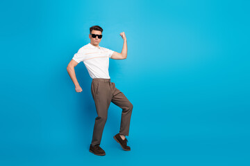 Confident young man in casual outfit striking a playful pose against a blue backdrop showcasing style and attitude