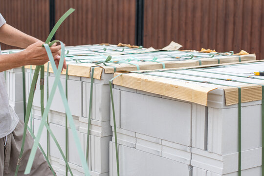 Person's hands unstrapping a new pallet of white aerated concrete blocks, preparing insulation materials for a construction project, building a house or beginning home renovation work