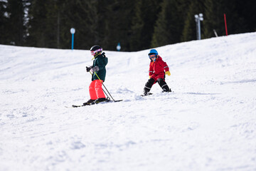 Children skiing downhill on sunny winter day