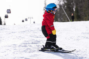 Child skiing downhill on sunny snowy slope near ski lift