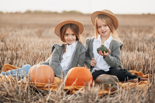 Two girls in hats enjoying pumpkins in a field during autumn sunset
