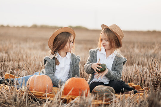 Two girls in hats enjoy pumpkins during a harvest day in a sunny field in autumn