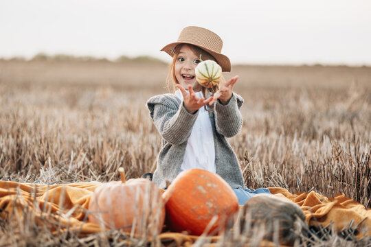Child enjoying autumn harvest in a pumpkin field while holding a small pumpkin with excitement at sunset