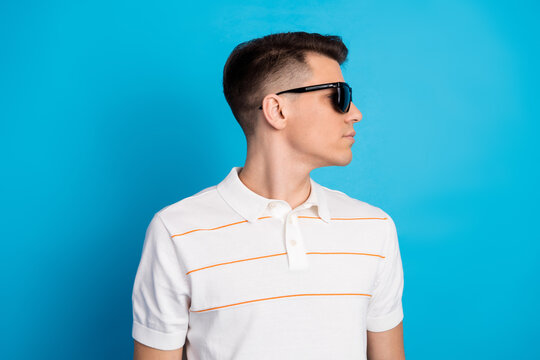Confident young man in a casual striped polo shirt wearing black sunglasses against a vibrant blue background in stylish pose