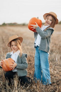 Two girls holding pumpkins in a golden field during autumn evening, showcasing the joys of harvest season