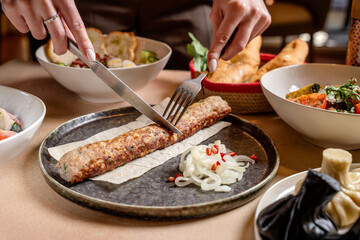 Cutting Georgian lula kebab with fork and knife at table