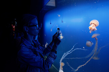 A person taking a photo of jellyfish in an aquarium with a smartphone.