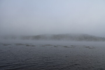 A dense morning fog sitting over the water of a lake in the wilderness. 