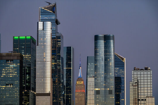 View of glassy skyscrapers pierce the twilight sky, their illuminated windows mirroring city lights, a majestic skyline rising in the dusky evening, Hudson Yard, New York, United States.