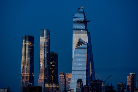 View of towering skyscrapers pierce the twilight sky, their glass facades reflecting the last light of day, creating a stunning urban silhouette, Hudson Yard, New York, United States.