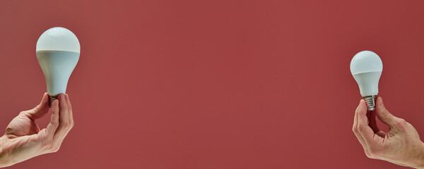 Two hands holding different size led light bulbs on red background representing energy saving and eco friendly solutions