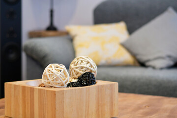 Wooden box with two-colored straw balls as decoration. The room is the living room where you can see a sofa with cushions.