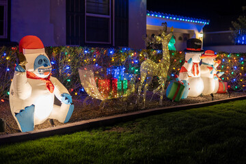 Luminous inflatable figures of abominable snowman, Snowmen family, Deer figure with gifts glowing at night. Outdoor Christmas decorations in the yard