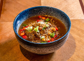 Spicy Sichuan Beef Noodles in Dark Broth Topped with Chili, scallions and Crushed Peanuts on wooden table side view of Chinese food