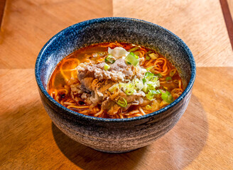 Spicy Hot Pot Style Ramen Noodles with Thinly Sliced Beef and Scallions in broth on wooden table side view of Chinese food