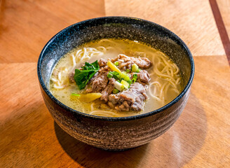 Spicy Beef Brisket and Pickled Pepper Noodle Soup in a Rich Broth with Scallions on wooden board side view of main course
