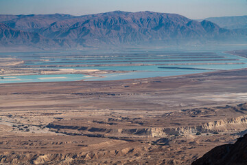 Jerusalem, Israel - 31 October 2019: View of the Dead Sea's azure waters contrasting with the arid, sun-baked desert landscape, and distant mountains rise against the clear sky.
