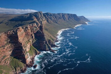 Fototapeta premium A high-altitude view showcases a dramatic coastline with rugged, red cliffs meeting a vast expanse of blue ocean.