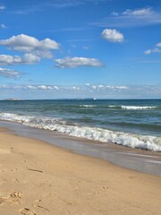 sandy coastline with breaking surf and cumulus clouds