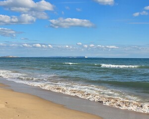 Blue ocean waves breaking on the sandy beach with a distant coastline