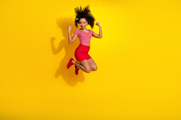 Obraz premium Joyful woman in stylish attire leaping against a vibrant yellow background celebrating happiness with energy and style