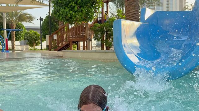 Girl in pink goggles sliding into refreshing pool capturing carefree holiday moment of fun summer family travel
