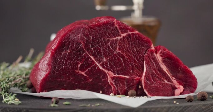Fresh raw beef meat with pepper and thyme turning on dark wooden cutting board