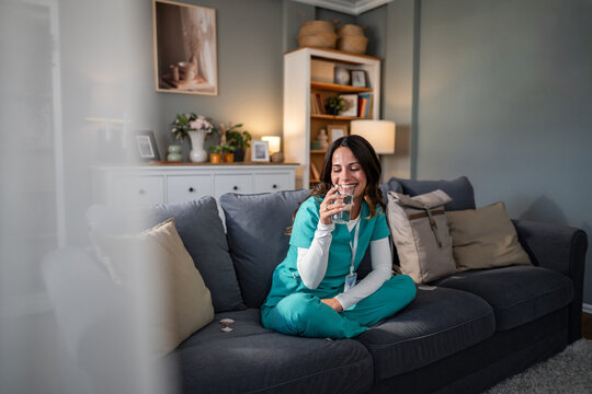 Nurse relaxing home hydrating with glass of water - Powered by Adobe
