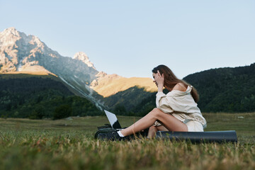 Naklejka premium A relaxed woman sits on a mat in a wide meadow with a laptop, enjoying sunny weather and peaceful scenery, conveying focus, creativity, and a productive outdoor work mood.