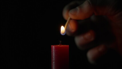 Match lighting single candle isolated on black background. Wick lights up flame