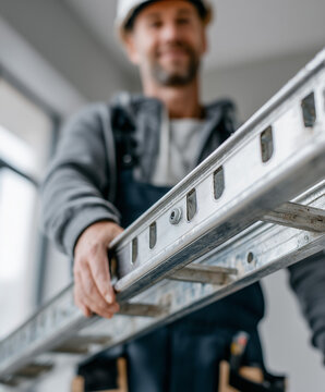 Trabajador con casco de seguridad y escalera met&aacute;lica en entorno interior iluminado, realizando tareas de mantenimiento o construcci&oacute;n con equipo de protecci&oacute;n personal y actitud profesional.