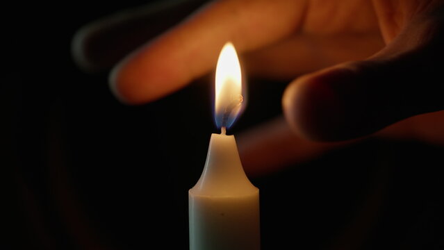 Fingers squeezing candle fire on black background closeup. Person snuffing wax