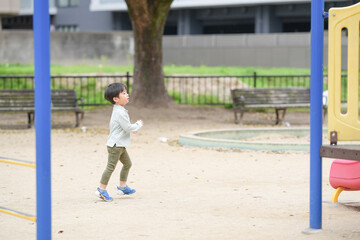 A young boy is playing in a park with a blue and yellow swing set. The boy is wearing a blue and white shirt and blue shoes