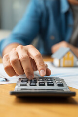 Calculating Home Finances: A person is using a calculator to analyze financial documents with a small house model in the background.