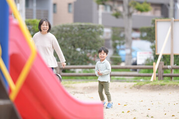 Obraz premium A woman and a child are playing in a park. The woman is holding the child's hand and they are both smiling. The park has a red slide and a fence