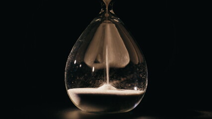Elegant hourglass measuring minutes in dark room closeup. Macro sand falling