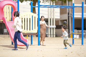 A woman and two children are playing in a park. The woman is wearing a brown dress and the children...