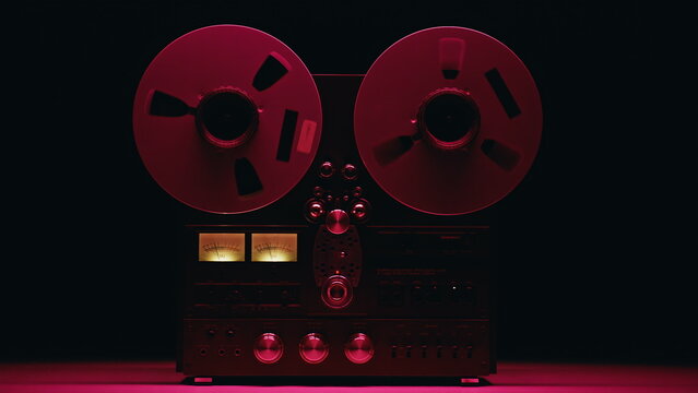 Hand turning reel-to-reel device at red neon light illuminated room closeup. 