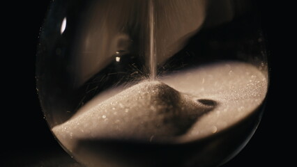 Gold sand flowing hourglass standing in evening light at dark background closeup