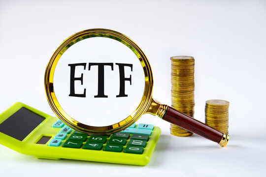 ETF - acronym under magnifying glass on the background of calculator and stack of coins