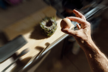 A chicken egg in a hand. A bird's nest in the table at the background. Kitchen interior. 